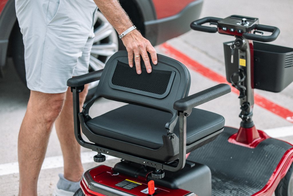A person folds a red Hoverfly T5 foldable mobility scooter before a long-distance journey.