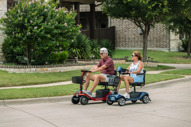 Two seniors ride Hoverfly T5 and T4 four-wheel mobility scooters for stable outdoor travel on a residential street.