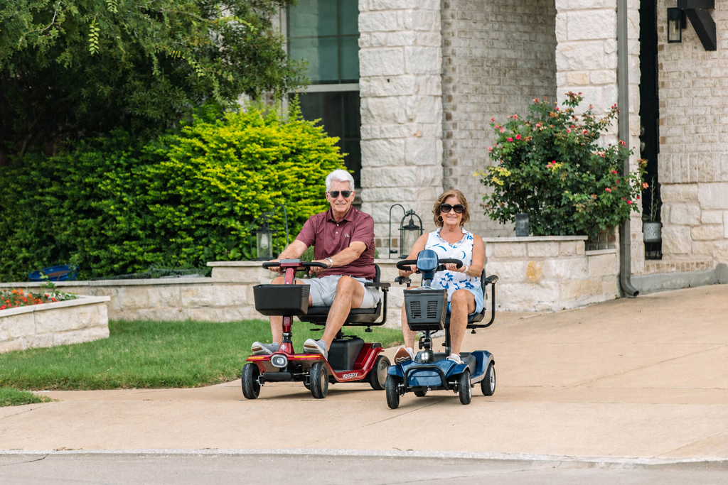 Older couple riding Hoverfly T4 and T5 mobility scooters on a gently sloped residential driveway.