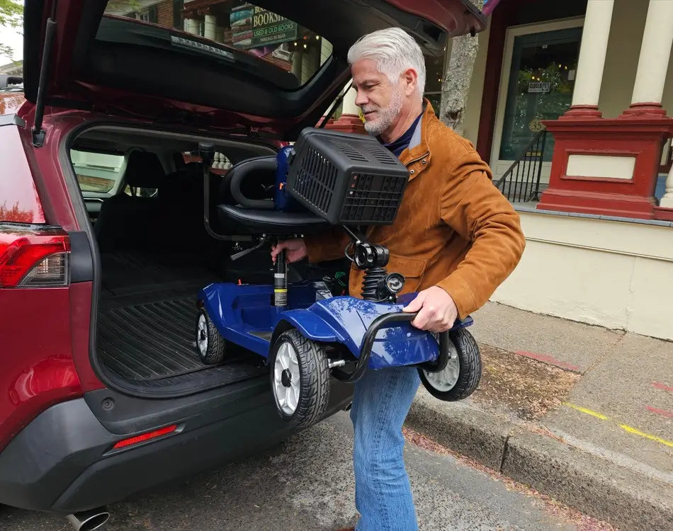 a man is lifting a folded mobility scooter