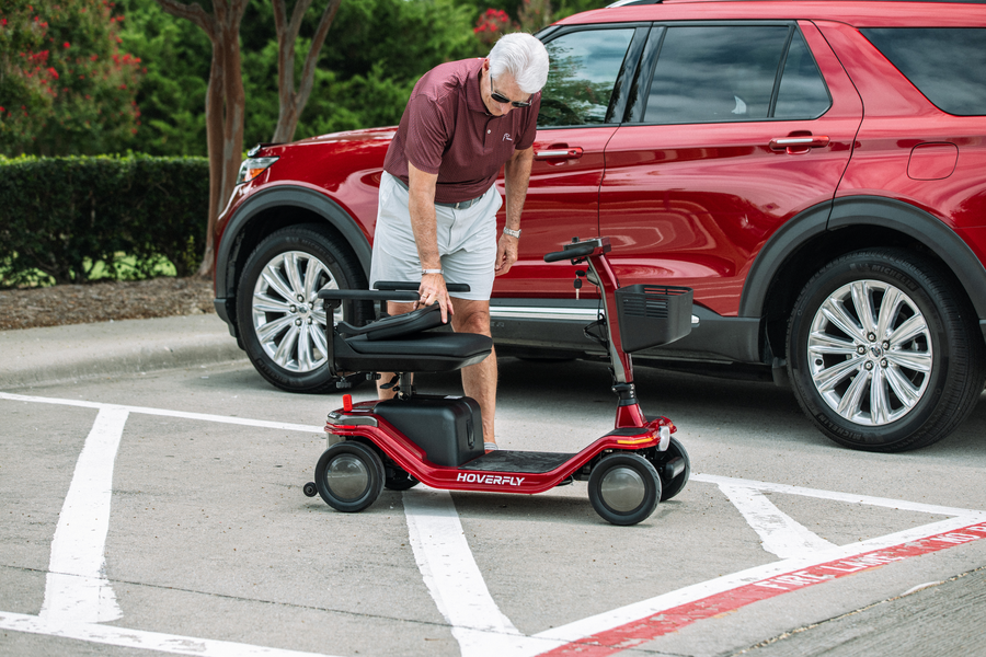 Senior man folds the Hoverfly T5 four-wheel mobility scooter before loading it into a car trunk.