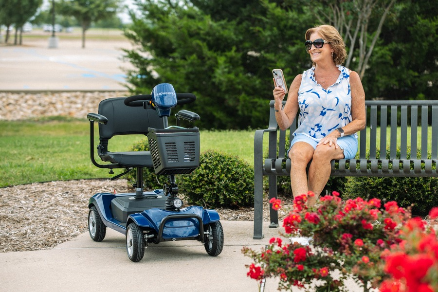 Senior traveler rests beside a Hoverfly T4 four-wheel mobility scooter during a comfortable, active outdoor trip.