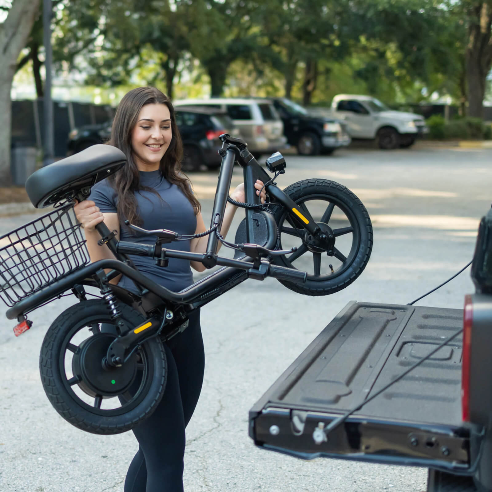 Woman carrying a black electric bike in a parking lot.